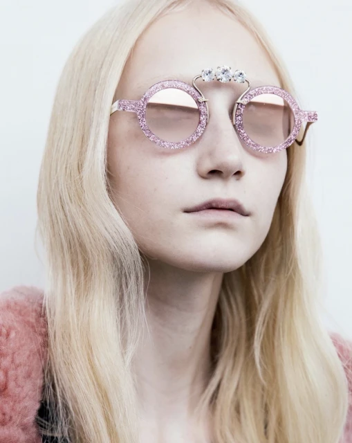 Close-up of a woman with blonde hair wearing pink glitter sunglasses with decorative jewels. Fashion and beauty product shot.