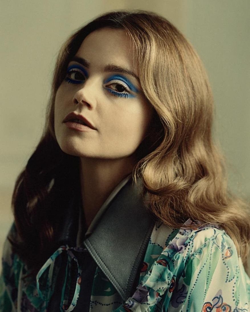 Close-up studio portrait of a female adult with wavy brown hair, wearing colorful floral top and striking blue eye makeup.