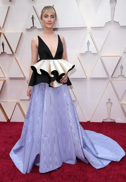 Fashionable woman in gown poses on red carpet at awards ceremony. She wears a black, white, and light blue dress and has blonde hair.