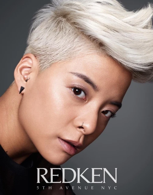 Close-up of a stylish adult female with platinum blonde pixie cut, wearing a nose ring and earrings. Shot in a photo studio.