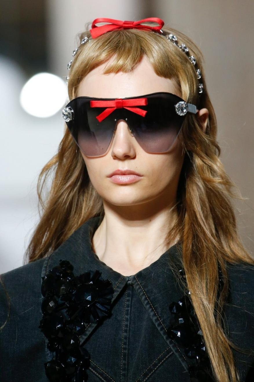 Fashion model wearing sunglasses with red bow and jeweled headband. Blonde hair, denim jacket. Beauty shot.