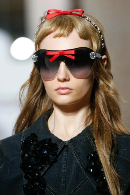 Fashion model wearing sunglasses with red bow and jeweled headband. Blonde hair, denim jacket. Beauty shot.