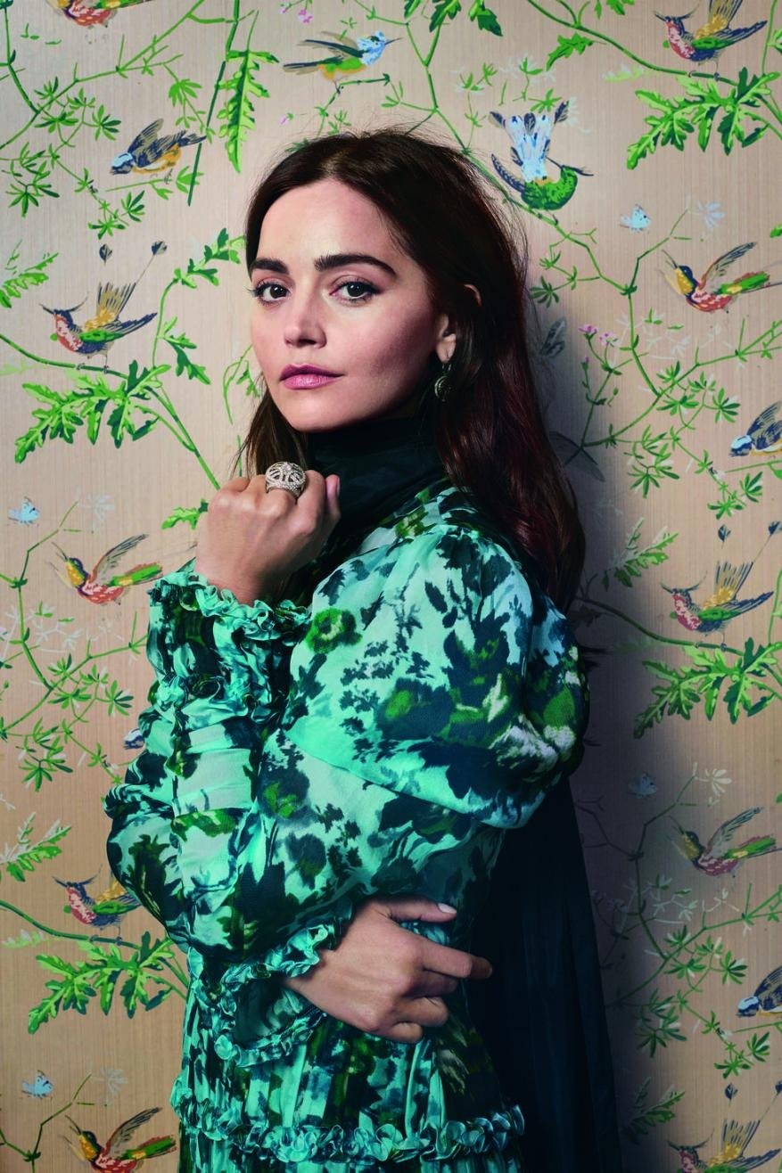 Close-up portrait of a female adult wearing a green floral dress against a bird-patterned wallpaper, showcasing fashion and style.