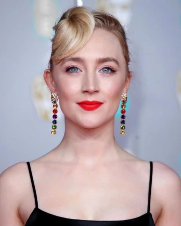 Portrait of Saoirse Ronan wearing dangling multi-colored gemstone earrings and a black dress with thin straps