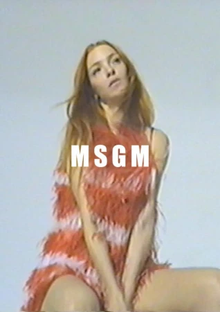Model with long brown hair wearing a fringed red dress against a light grey seamless backdrop