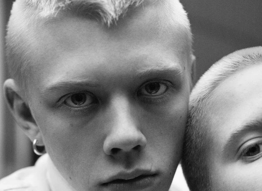 Black and white close-up portrait of two young adult males with short blonde hair, facing forward with direct eye contact.