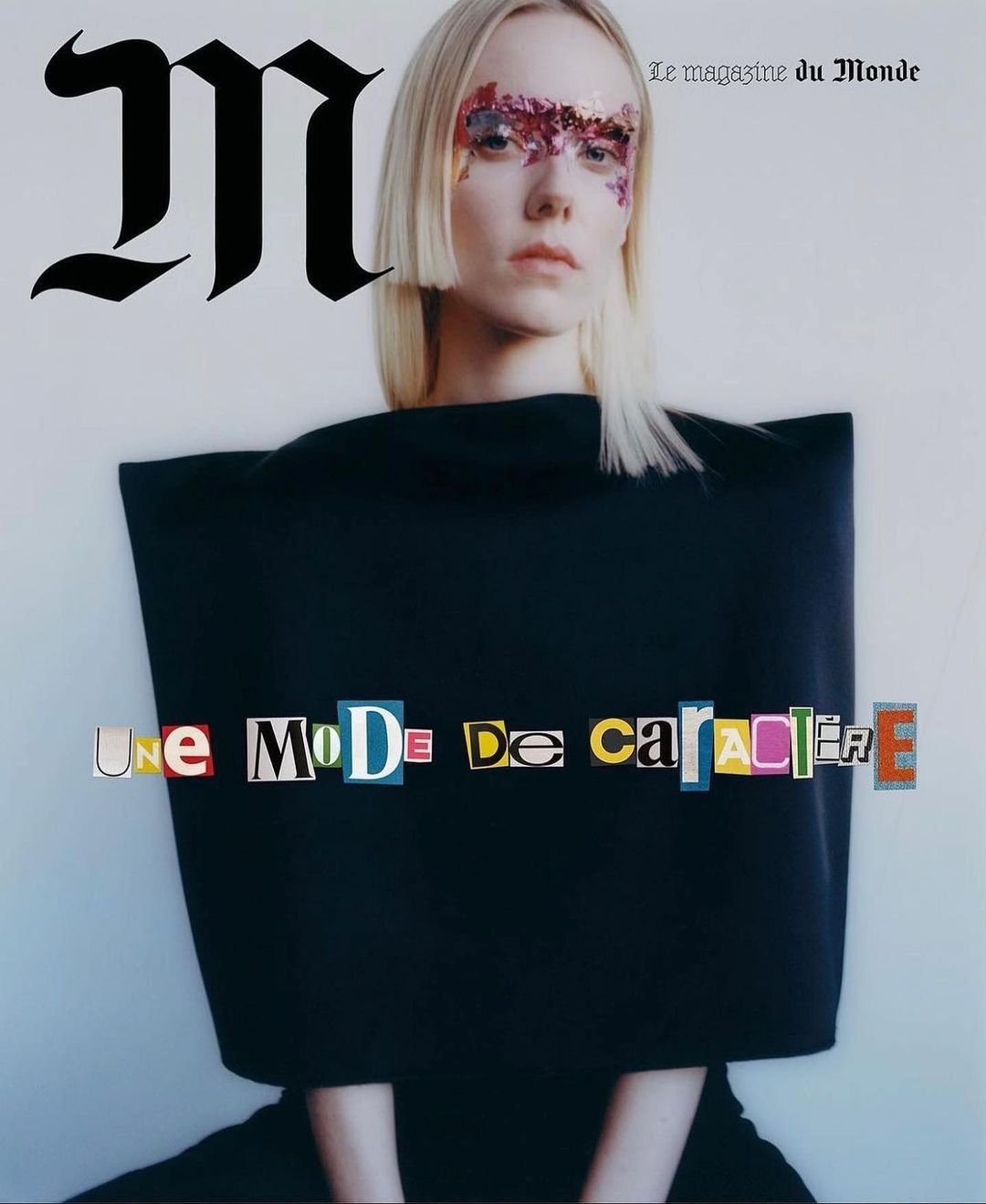 Magazine cover featuring a blonde woman with floral face art, wearing a modern black dress, against a plain background.