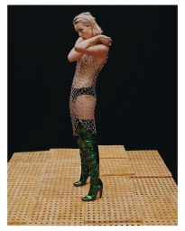 Model with slicked-back blonde hair wearing a sheer crystal-mesh dress and glossy green thigh-high boots.