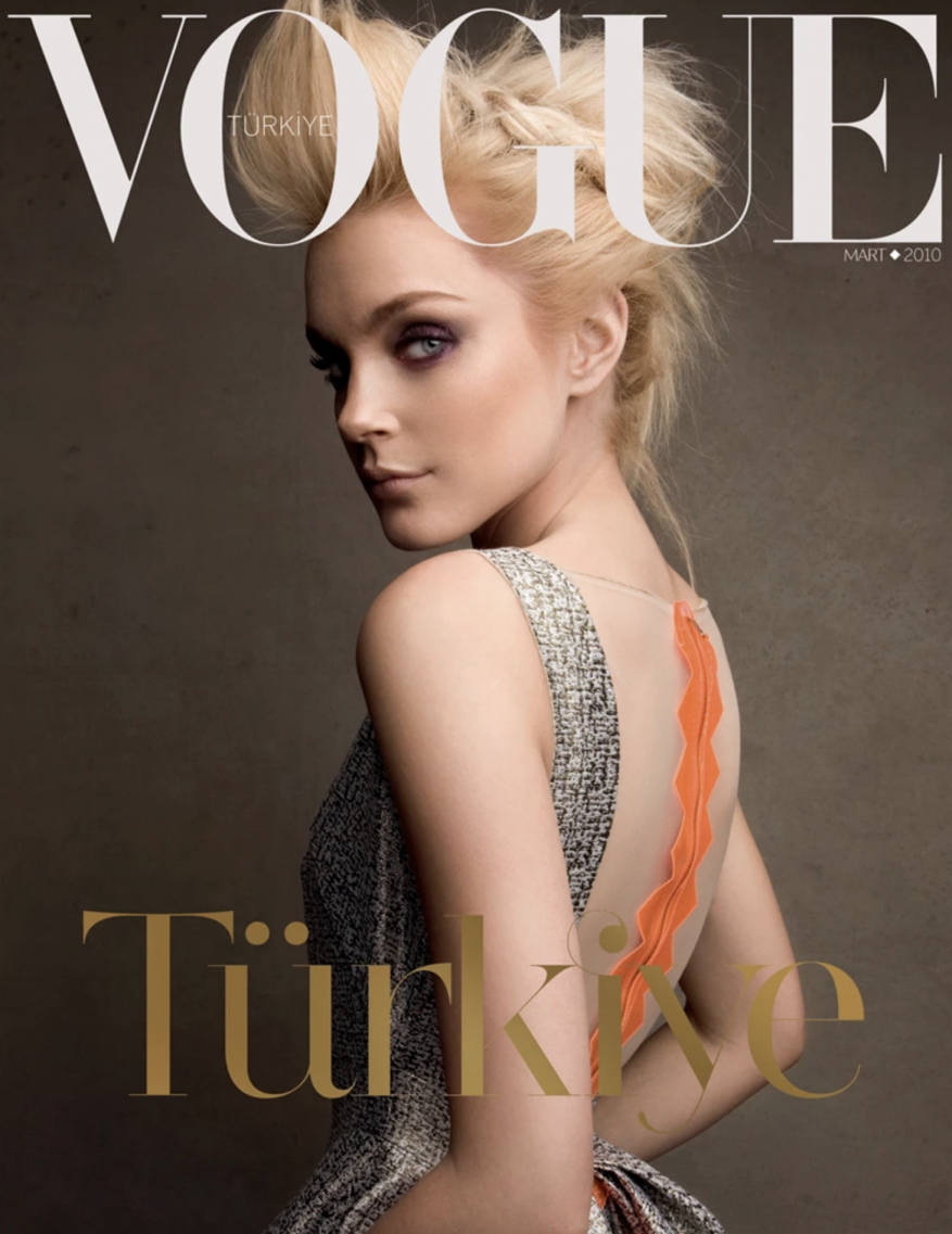 Vogue Türkiye magazine cover featuring a blonde woman with braided updo, wearing an open-back dress and bold eye makeup, against a grey backdrop.