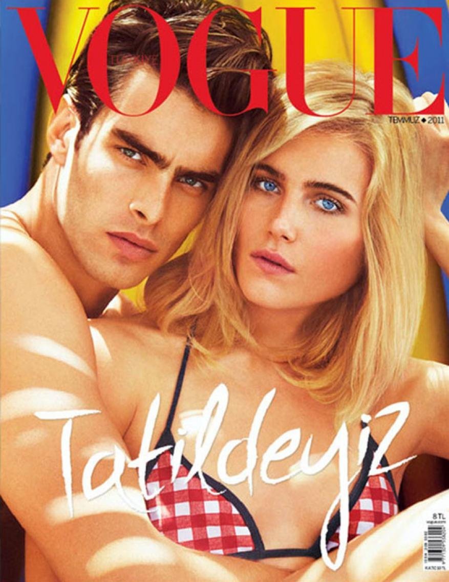 Fashion magazine cover featuring a brunette man embracing a blond woman wearing a red-and-white bikini top, with the VOGUE logo at the top.