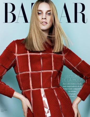A blond woman wearing a structured red checkered top poses against a solid light blue background for a magazine cover.