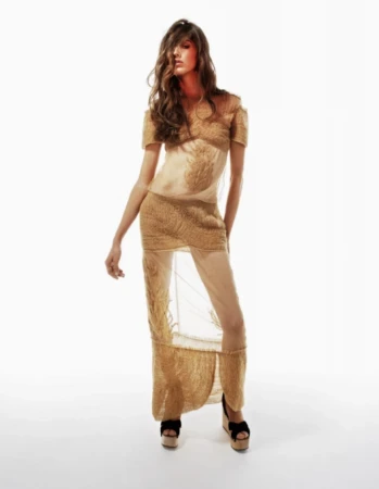 Model wearing sheer gold textured dress and platform wedge sandals against a white studio background.