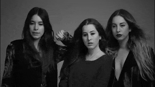 Three young adult women pose in a black and white studio shot, showcasing dark clothing and long hair against a plain background.