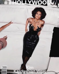 Kim Kardashian West lying on a white bed wearing a black strapless sequin dress and pearl necklace.