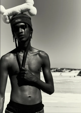 Shirtless man wearing a dark beanie with chin straps and a large plush bone balanced on his head against an outdoor backdrop.