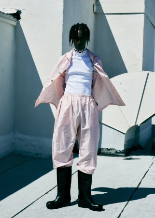 Model wearing a pink matching set with black boots standing on a rooftop under harsh natural light styled by Mecca Cox