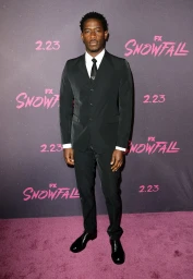 Damson Idris wearing a black suit on a purple carpet styled by Mecca Cox