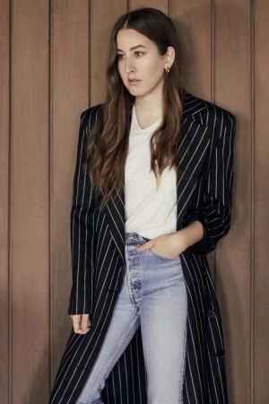 Woman in pinstripe coat and jeans leaning against wood paneling by Melissa Rogers