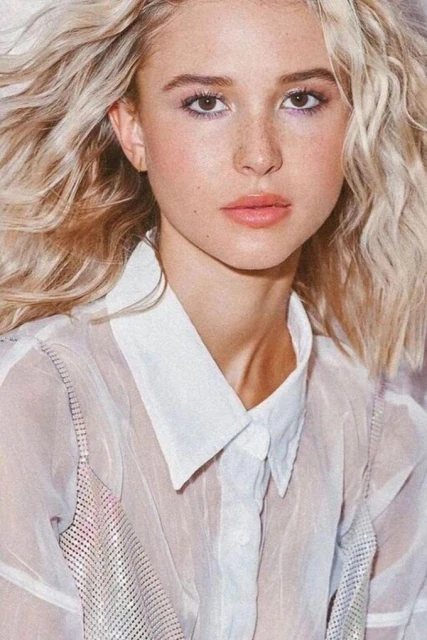 Close-up studio portrait of a young blonde woman in a sheer white blouse with fair skin and freckles looking at the camera.
