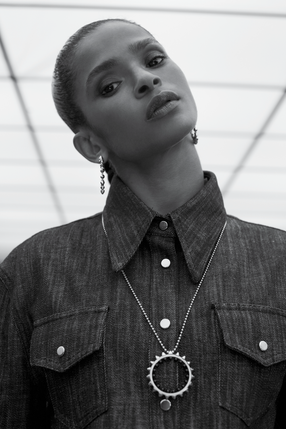 Black and white portrait of an African American woman in a denim shirt and silver necklace, posing against a white geometric background.