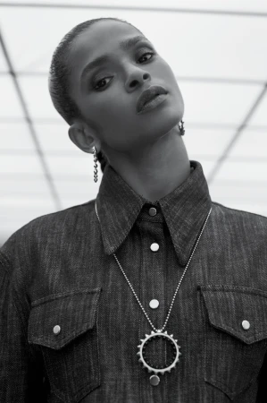 Black and white portrait of an African American woman in a denim shirt and silver necklace, posing against a white geometric background.