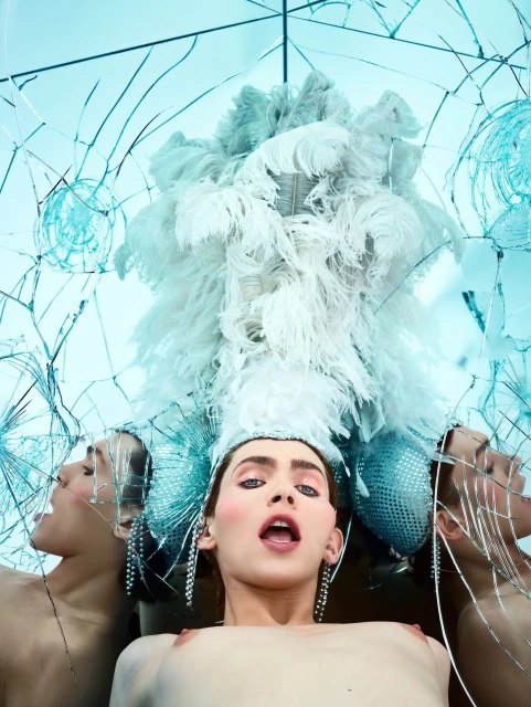 Surreal fashion portrait featuring a central person in feathered attire flanked by two side figures in a studio setting, shot through broken glass.