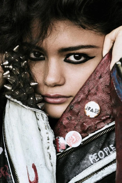 Close-up portrait of a young adult woman with dark hair, striking eye makeup, and a studded leather jacket with pins.