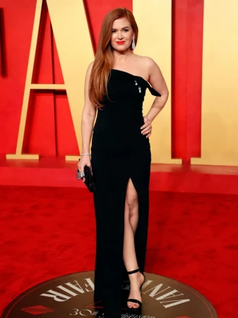 Isla Fisher poses on a red carpet wearing a black strapless gown and black high heels with a matching black clutch.