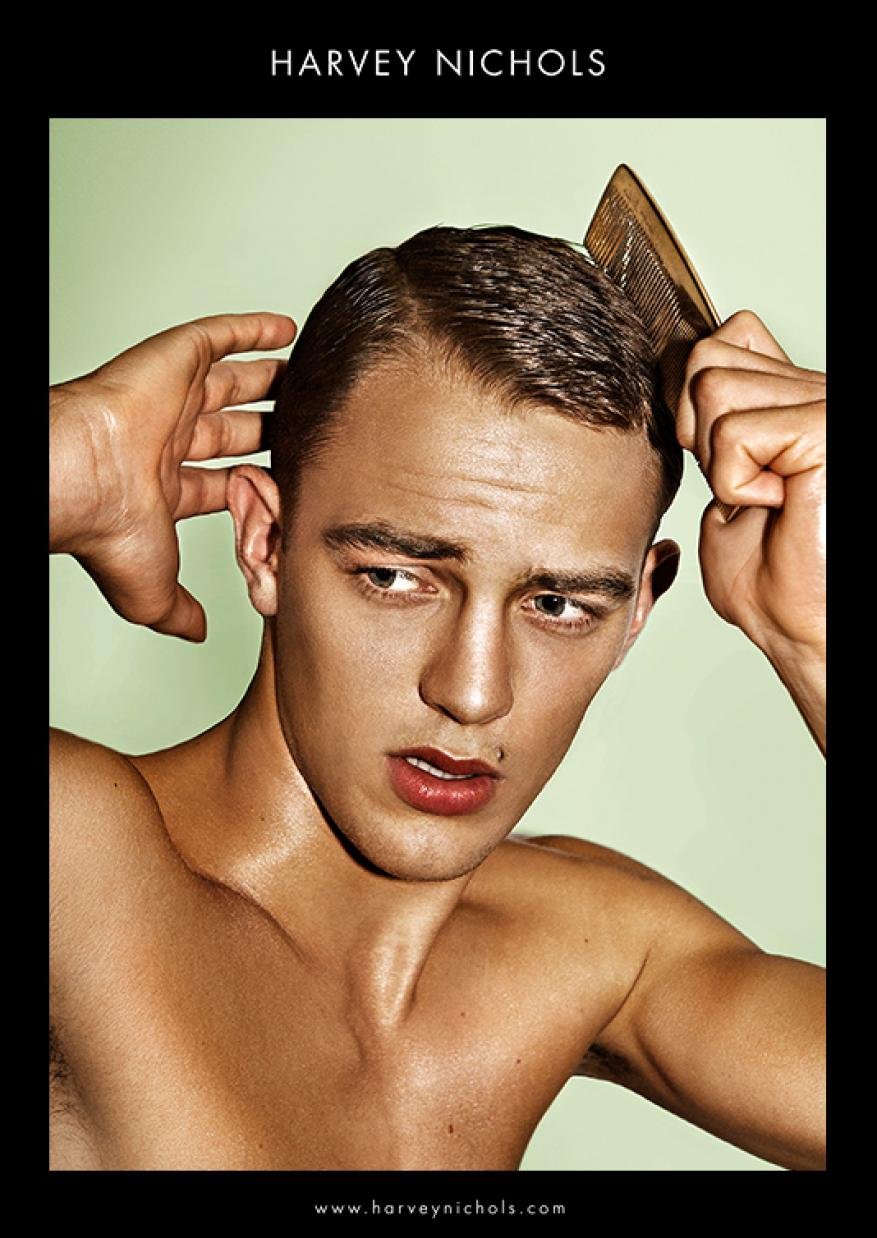 Nude male portrait in front of pale green background, combing his hair with a wooden comb, branded by Harvey Nichols logo.