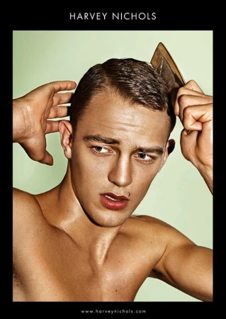 Nude male portrait in front of pale green background, combing his hair with a wooden comb, branded by Harvey Nichols logo.