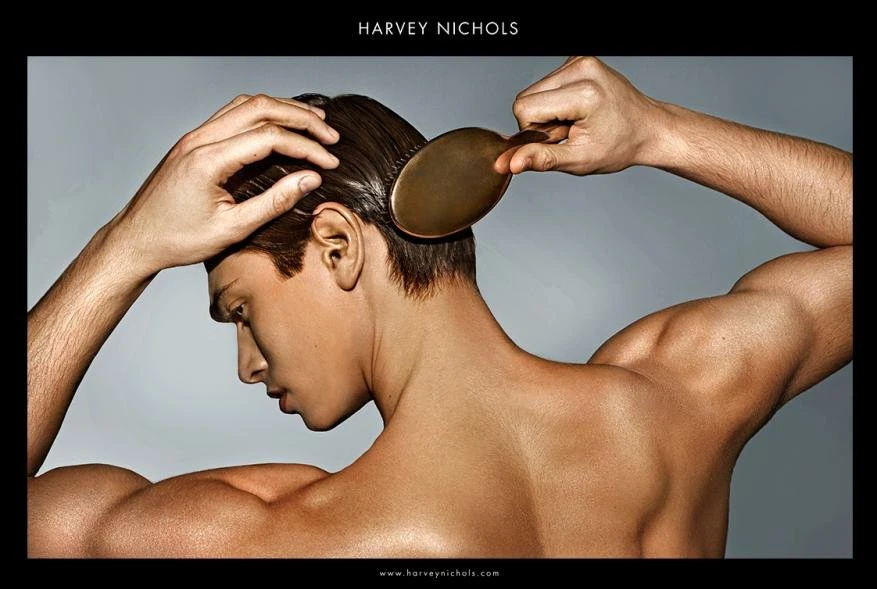 Close-up of a light-skinned adult male brushing his short, dark hair. The shot emphasizes grooming and fitness against a neutral backdrop.