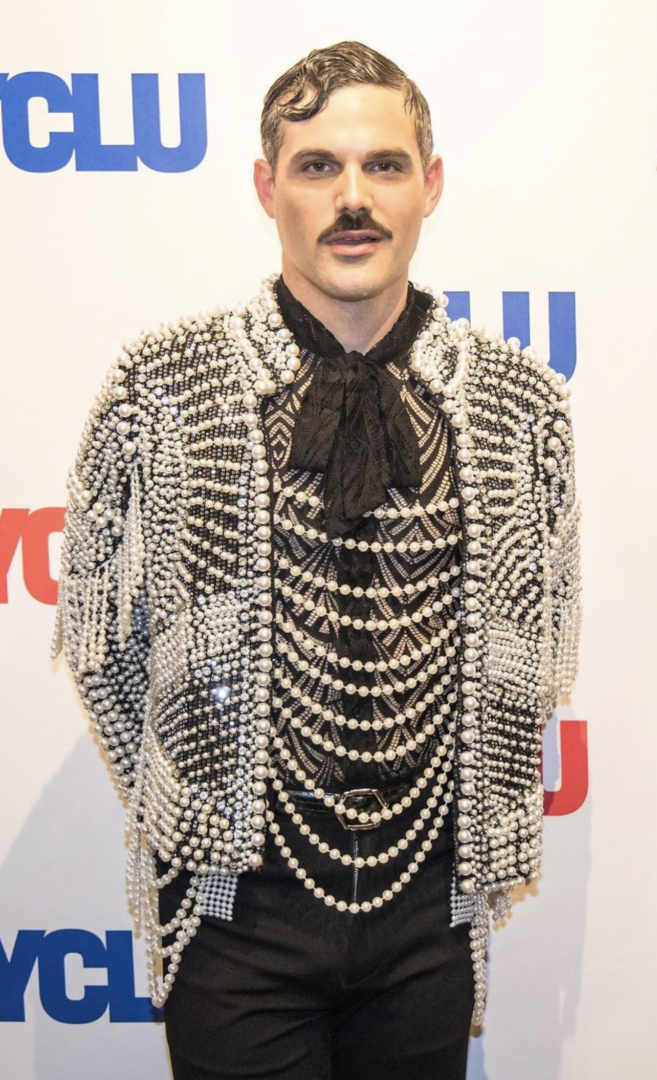 Adult male with a mustache wearing a pearl-covered jacket and black pants against a white background with text.