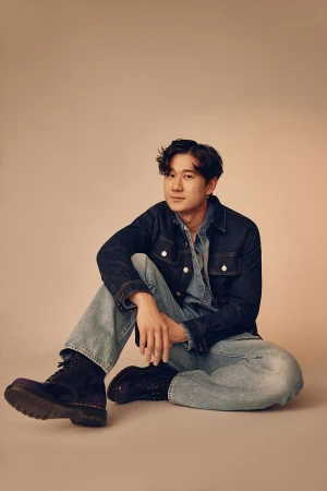 Man seated on a neutral backdrop wearing a denim jacket and jeans, styled by Michael Moreno.