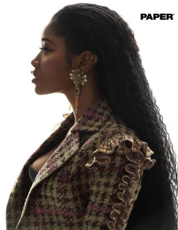 Profile portrait of a Black woman with long curly hair, wearing a patterned tweed jacket, and large jeweled earrings against white.