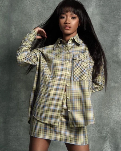 Young woman in plaid top and skirt posing against textured background; dark hair, looking at camera, studio lighting, fashion portrait.