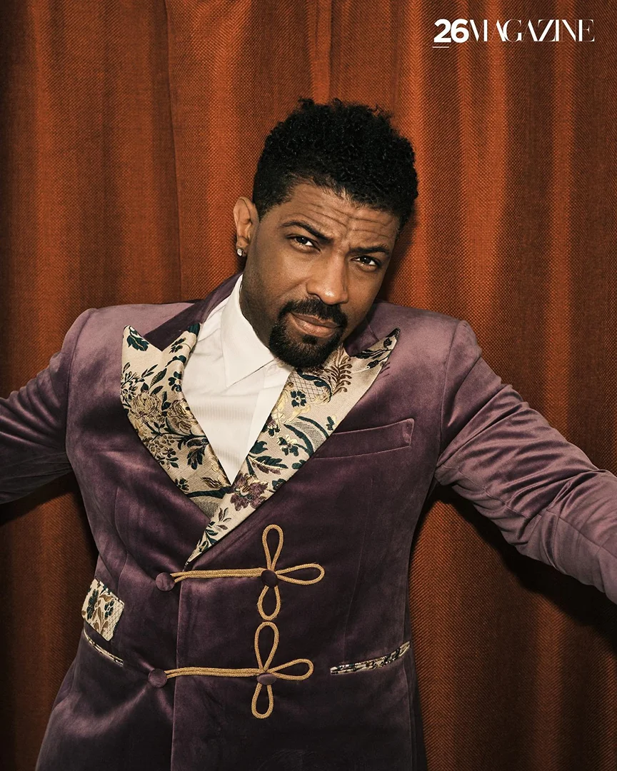 Headshot of a Black male model in a purple velvet suit with floral lapels posing in front of a brown curtain with text in the upper-right corner.