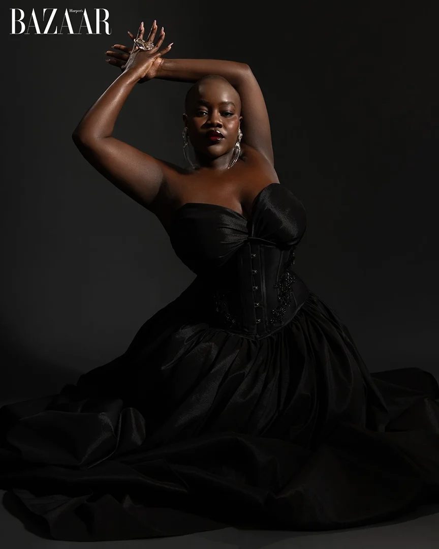 Glamorous portrait of a woman in a black dress, arms raised, adorned with jewelry against a dark background, capturing elegance and style.