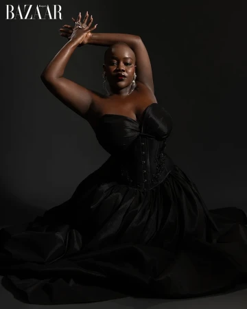 Glamorous portrait of a woman in a black dress, arms raised, adorned with jewelry against a dark background, capturing elegance and style.