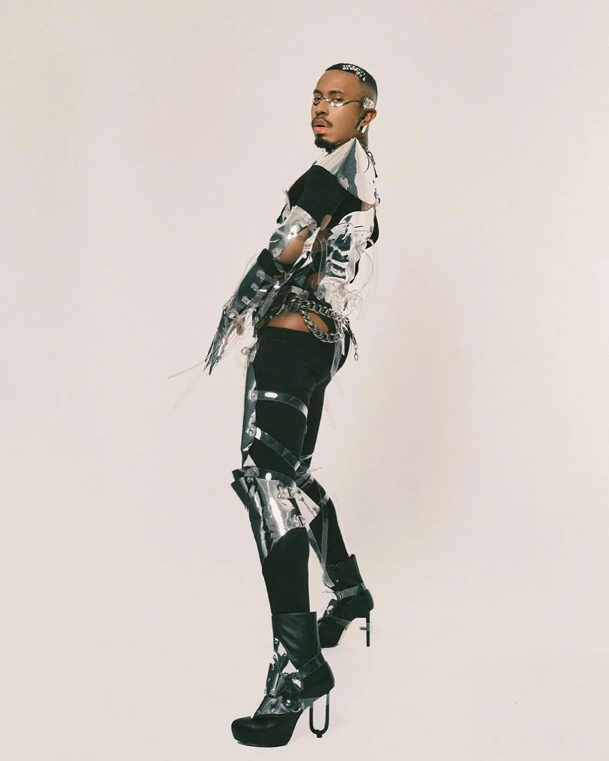 Person in futuristic silver fashion outfit poses in a studio, showcasing a unique and avant-garde style against a clean background.