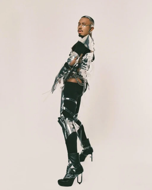 Person in futuristic silver fashion outfit poses in a studio, showcasing a unique and avant-garde style against a clean background.