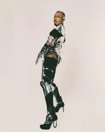 Person in futuristic silver fashion outfit poses in a studio, showcasing a unique and avant-garde style against a clean background.