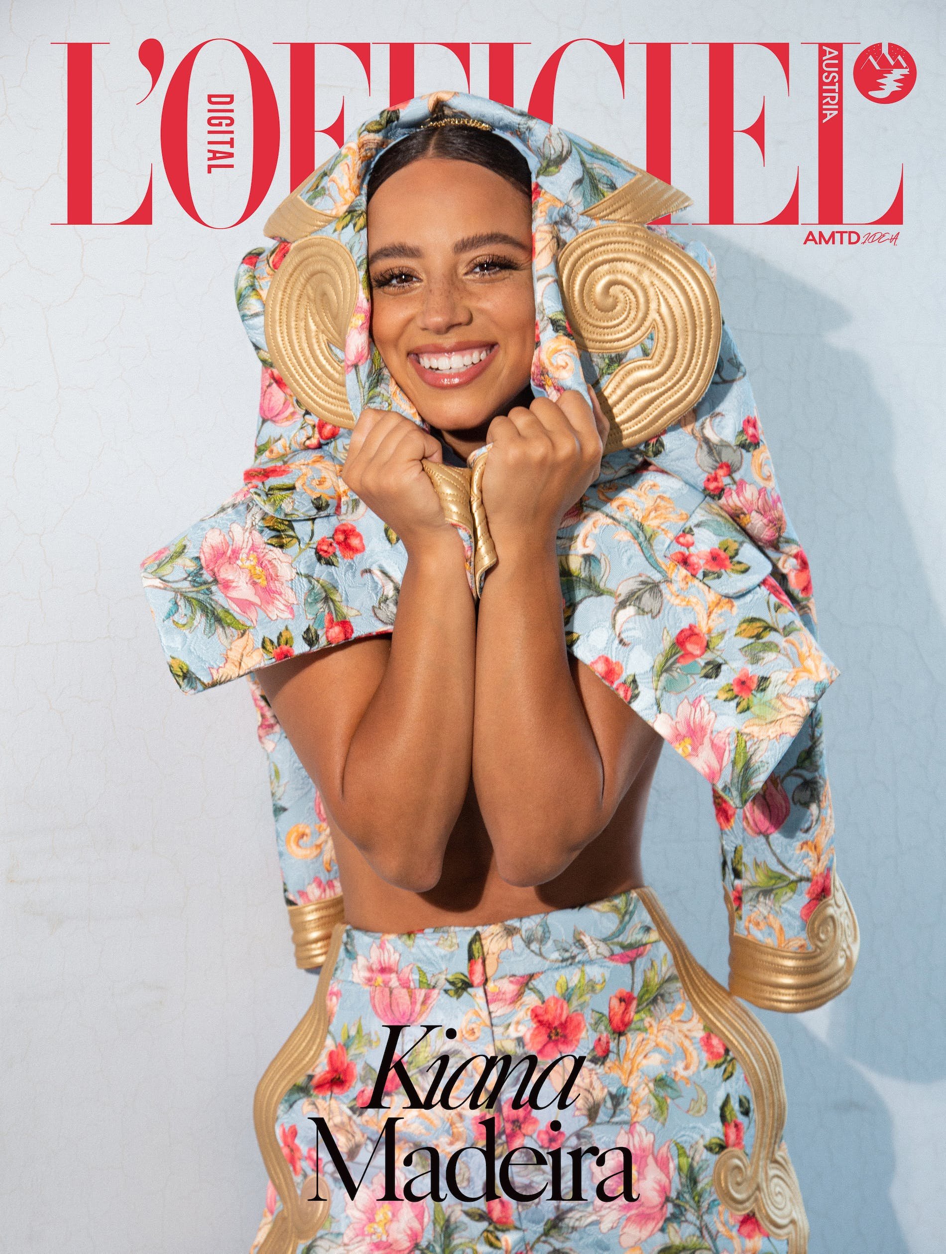 Magazine cover featuring a smiling woman with curly hair wearing a floral print outfit with decorative gold elements against a light backdrop.