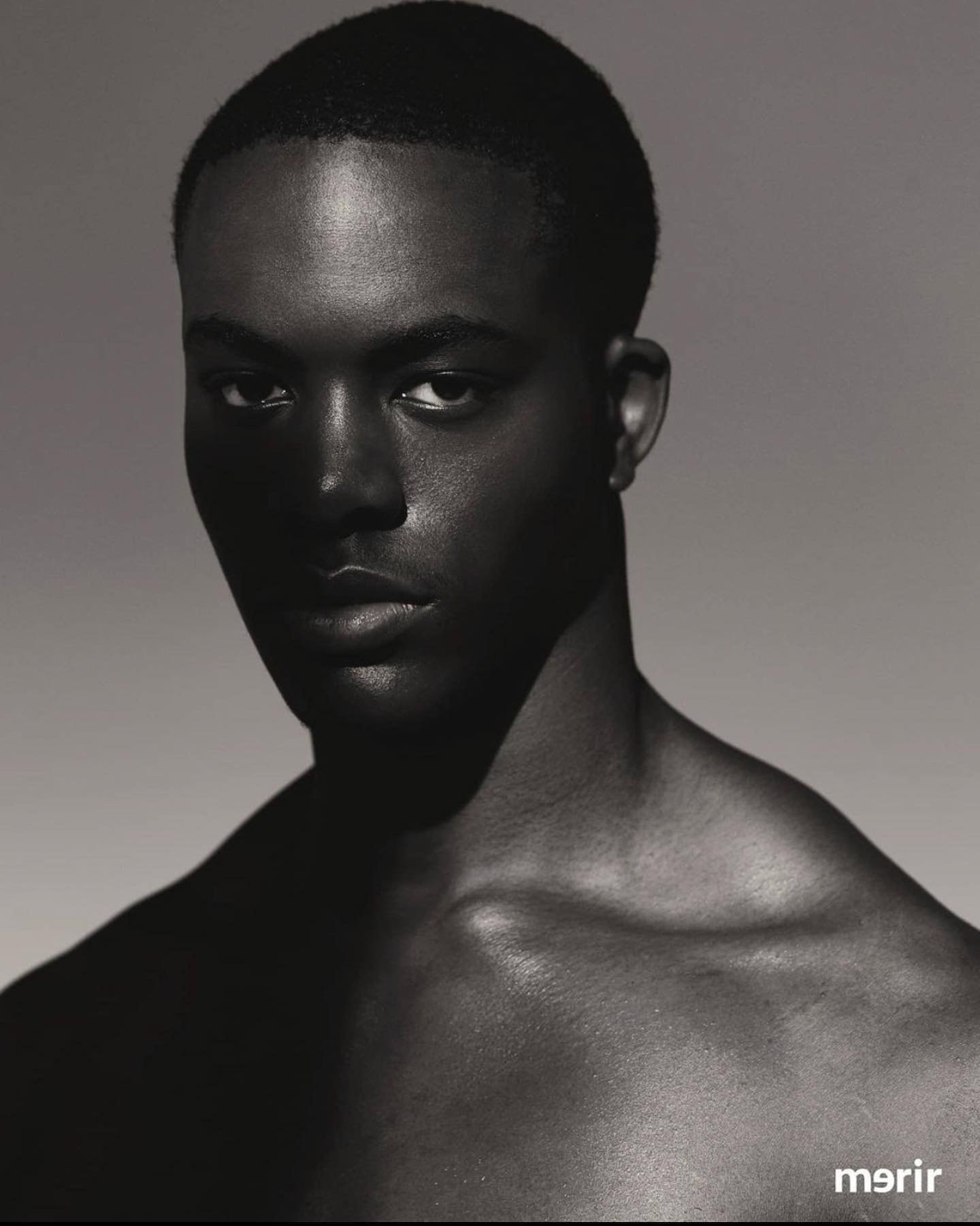 Close-up portrait of a shirtless Black man in a photo studio with a neutral background, showcasing beauty lighting and skin texture.