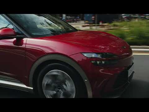 Dynamic low-angle shot of a moving red electric SUV on a city street, showcasing sleek design and urban environment.