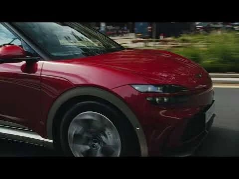 Dynamic low-angle shot of a moving red electric SUV on a city street, showcasing sleek design and urban environment.