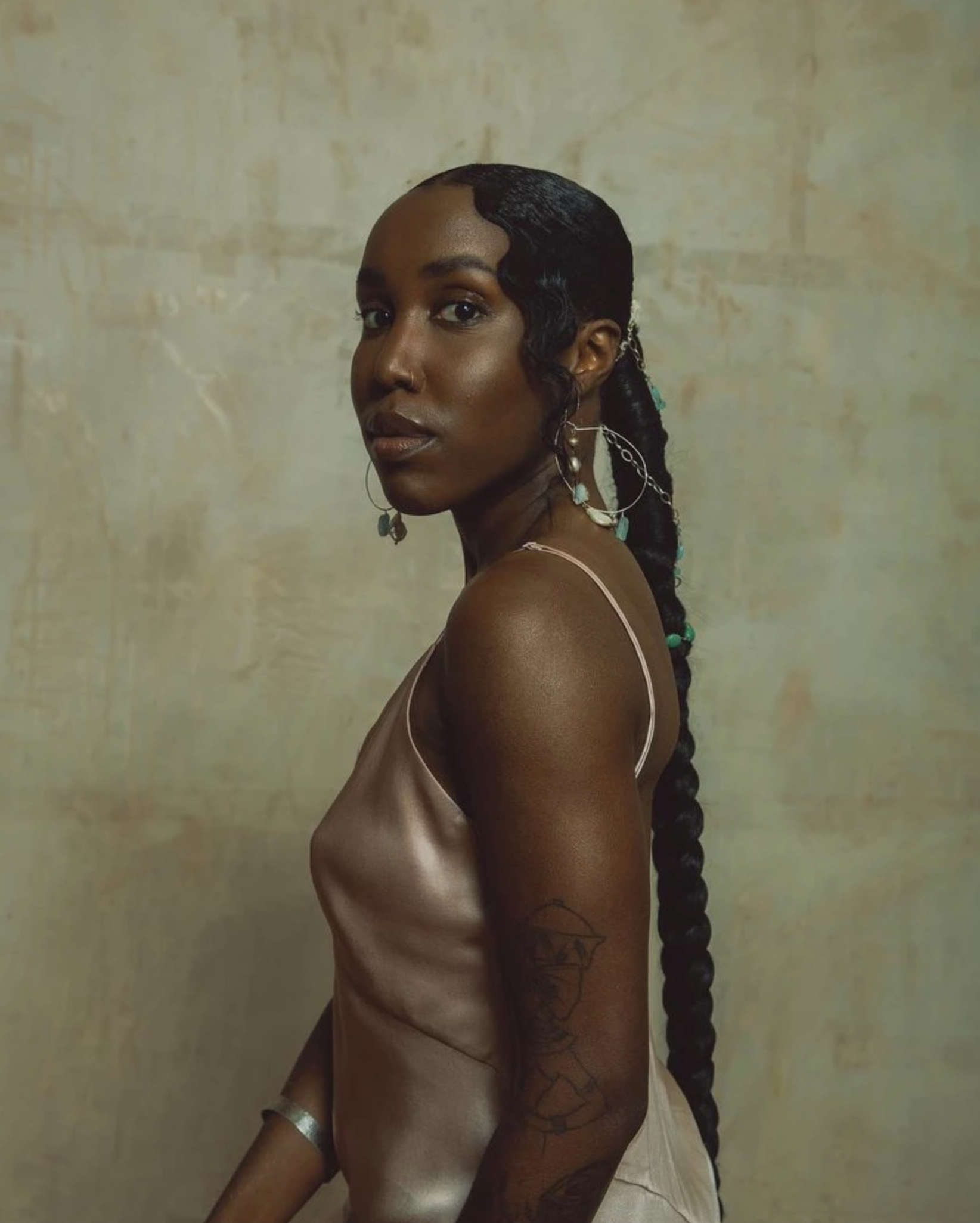Portrait of an adult woman with braided hair and a light pink dress posing in front of a textured mottled wall.