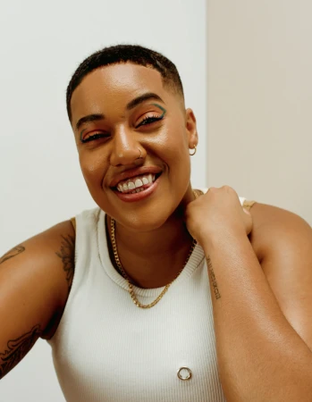 Close-up portrait of a smiling woman with short hair wearing a white tank top and gold chain necklace