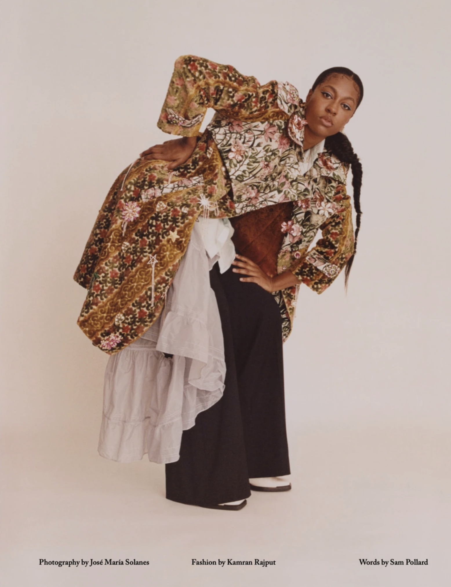 Fashion editorial shot of a woman in an ornate patterned jacket and black pants in a photo studio setting, captured in a medium shot.