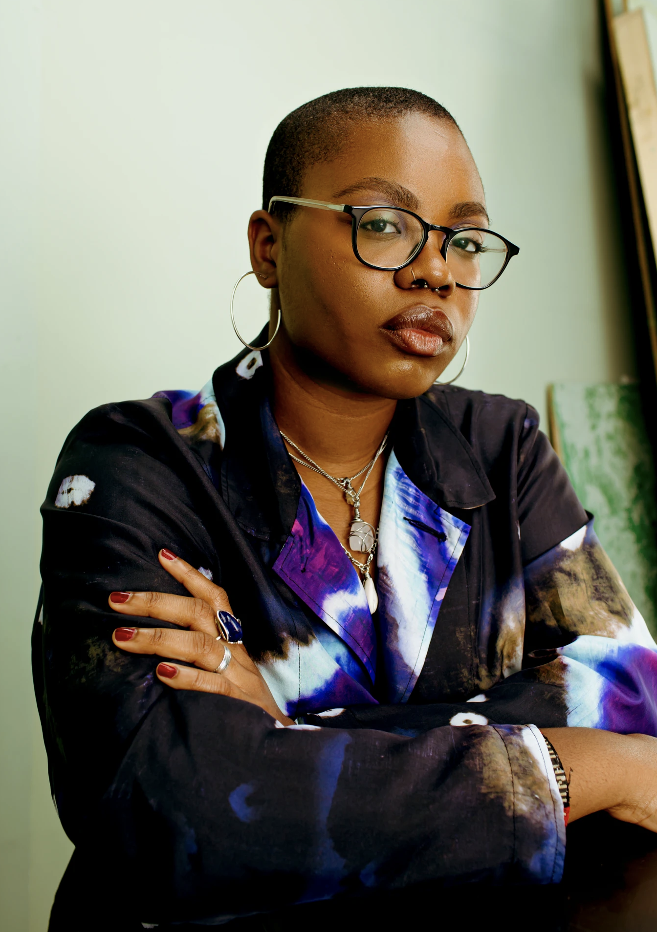 Portrait of a Black woman with short shaved hair wearing glasses and a patterned jacket with arms crossed.