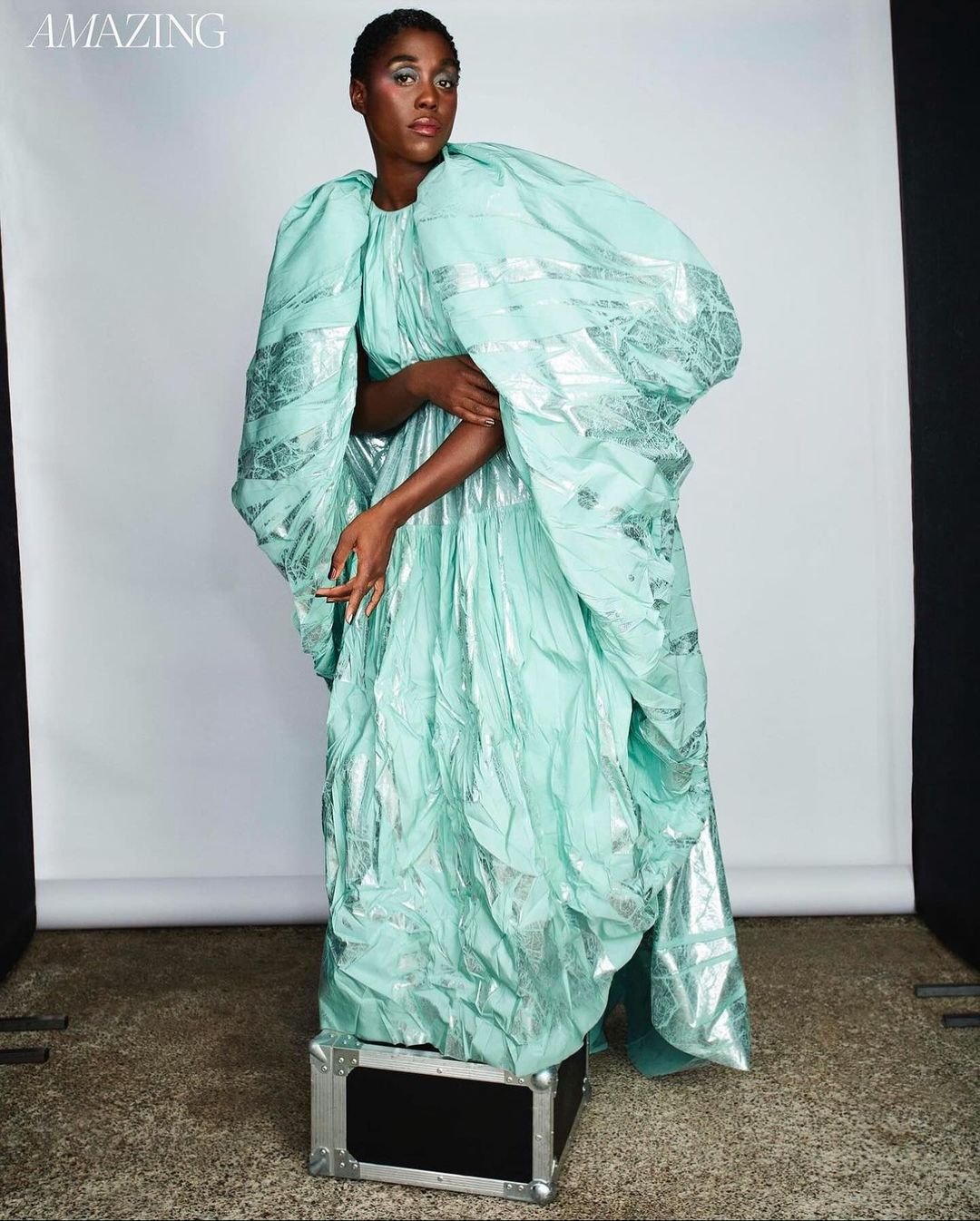 Black woman standing on a black case wearing a voluminous mint green dress with silver accents and dramatic puffy sleeves